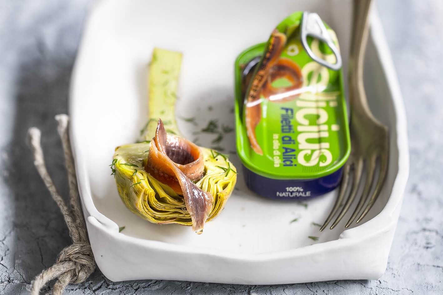 Delicius Anchovy in olive oil packaging with artichoke and anchovies on a white plate